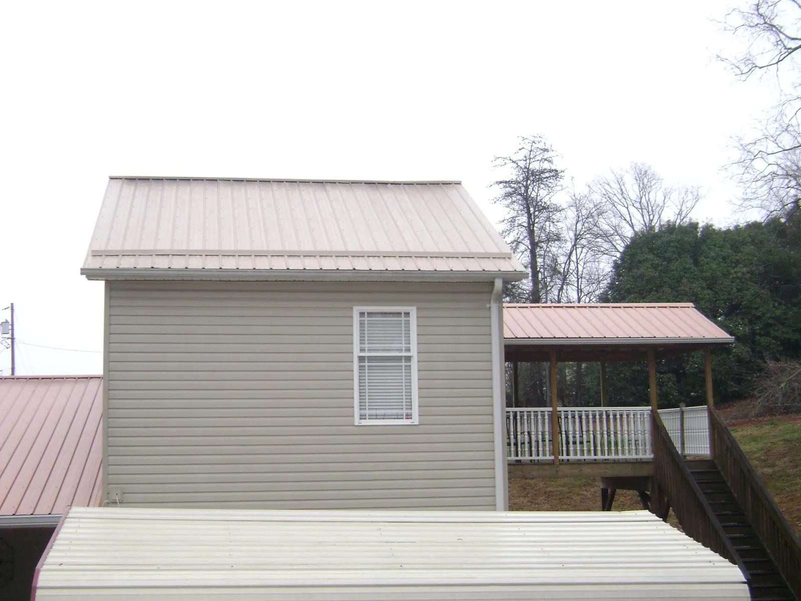 Tan metal roofs on a two story addition and attached porch, from a Roof Replacement job in Martinsville